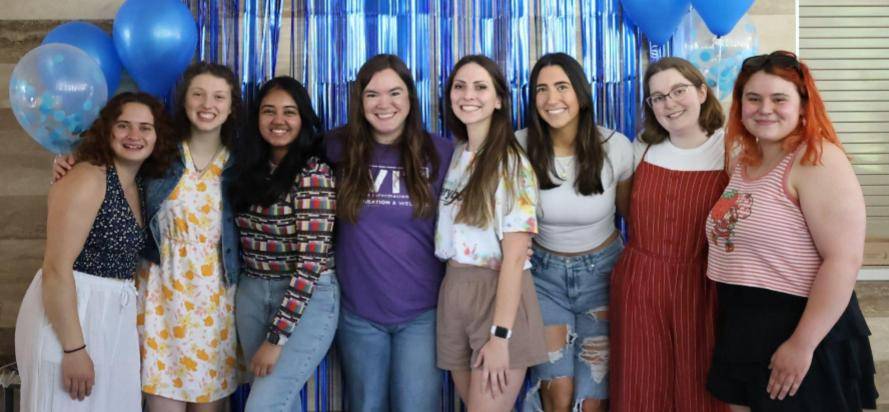 Peer educators and supervisor Katie posing for picture in front of blue backdrop and balloons